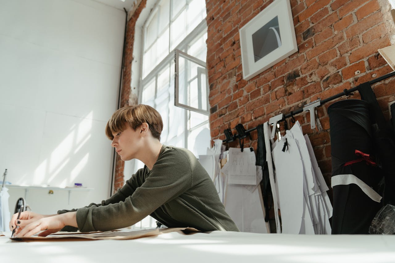 A focused female fashion designer working in a studio with a brick wall background.